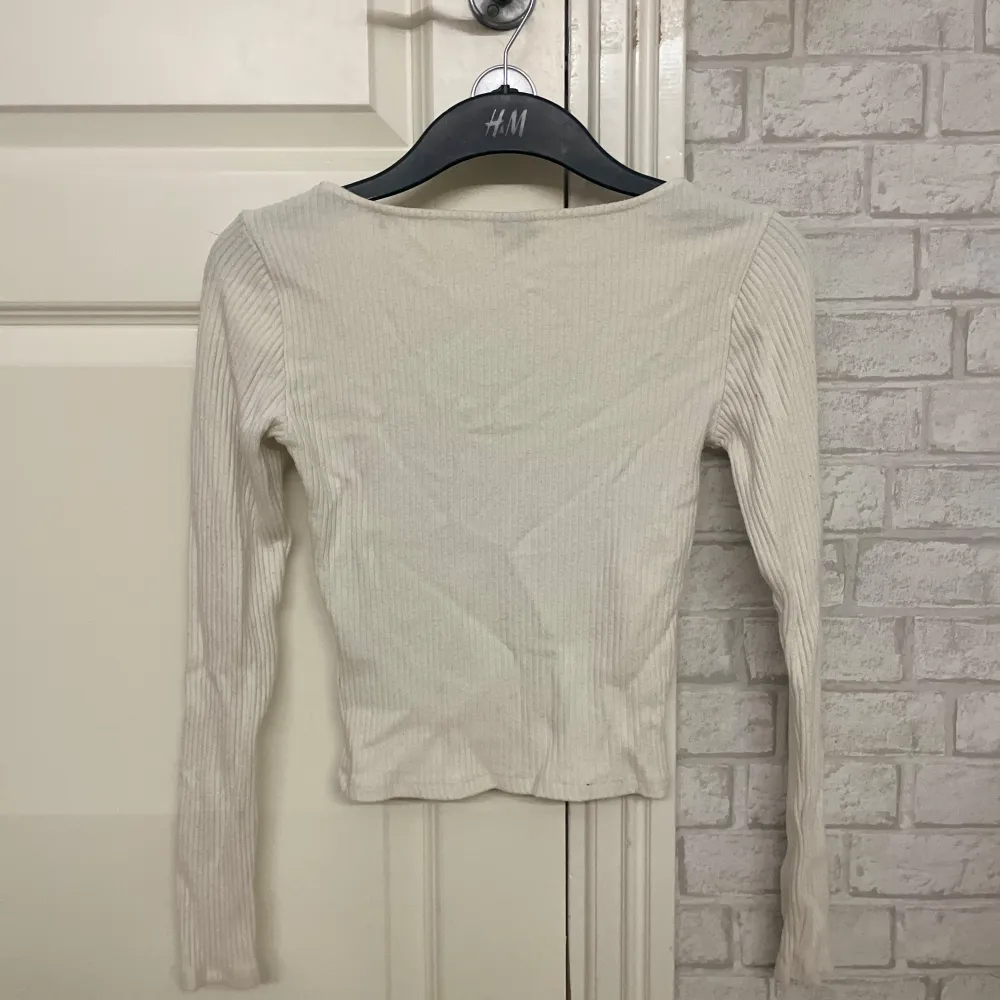 Säljer en stilren vit ribbad topp från H&M med långärmad design och fyrkantig halsringning. Perfekt för lager-på-lager eller som den är. Passar till många olika stilar och tillfällen.. Neuletakit & Villapaidat.