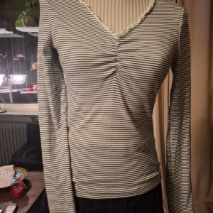 Randig långärmad topp från Holly & White - Snygg randig topp från Holly & White i svart och vitt. Den har en v-ringad design med rynkdetalj framtill och långa ärmar. Perfekt för en stilren look.