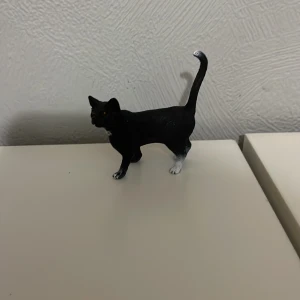 Schleich katt - En liten svart kattfigur med vita tassar och en uppåtstående svans. Perfekt för samlare eller som dekoration.