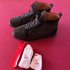 Svarta Louboutins - Snygga svarta sneakers från Louboutin med glittriga detaljer och klassisk röd sula. Skorna kommer ej till användning längre så därav säljer jag dom. Använt skick. Har tyvärr ej kvar boxen därav det billiga priset. Pris kan diskuteras vid snabb smidig affär.