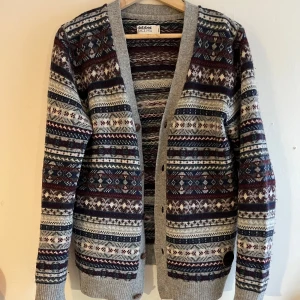 Vintage cardigan från Dobber - Säljer en snygg mönstrad kofta från Dobber i grått, vinrött och blått. Koftan har ett traditionellt mönster och knappar framtill. Perfekt för kyliga dagar med sin stickade design och långa ärmar ❄️🎿✅. Skriv vid funderingar😁