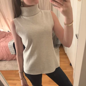 Beige ärmlös polotopp från Zara - Säljer en stilren beige ärmlös polotopp från Zara. Toppen har en hög ribbad krage och är perfekt för lager-på-lager eller som den är. Passar både till jeans och kjol för en chic look.