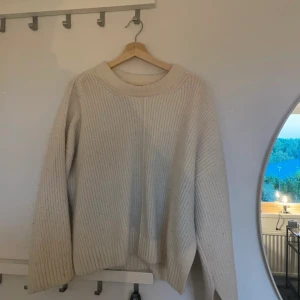 Vit stickad tröja - Säljer en mysig vit stickad tröja med ribbad struktur. Tröjan har en avslappnad passform och långa ärmar, perfekt för kyligare dagar. Den är enkel och stilren, vilket gör den lätt att matcha med olika outfits.