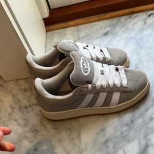 Grå sneakers från Adidas - Snygga grå campus sneakers från Adidas som jag köpte på Adidas i Paris sokorna är knappast använda. Skorna har vita ränder och snörning. Skorna har en bekväm passform och en gummisula. Perfekta för en avslappnad stil.