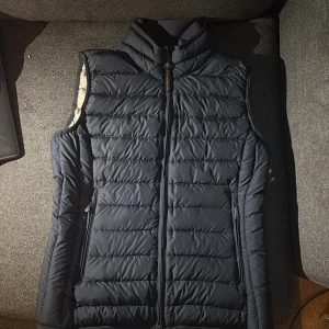 Mörkblå dunväst från Parajumpers - Säljer en snygg mörkblå dunväst från Parajumpers. Västen har en quiltad design med dragkedja och en praktisk säkerhetsficka på insidan. Perfekt för kyligare dagar när du vill hålla stilen. Kontakta mig för mer info!