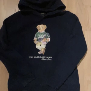Mörkblå hoodie  Ralph Lauren Polo Bear - Säljer en mörkblå hoodie från Ralph Lauren med det populära Polo Bear på framsidan. Hoodien har en klassisk design med huva. 