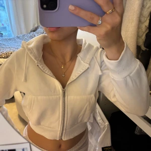 Vit croppad hoodie - Säljer en snygg vit croppad hoodie med dragkedja och luva. Den har långa ärmar och ribbade muddar vid ärmslut och nederkant.  Använt endast en gång.
