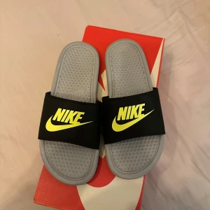 Nike Tofflor - Snygga och bekväma sandaler från Nike med en grå sula och svart rem. Den neongröna Nike-loggan på remmen ger en sportig touch. Perfekta för avslappnade dagar.