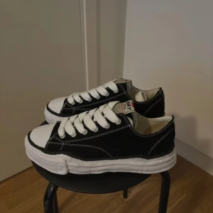 Maison Mihari Yasuhiro Sneakers  - Snygga svarta sneakers från MMY med vit sula och vita snören. Skorna har en klassisk design med rund tå och kontrasterande sömmar. Perfekta för en stilren look. 