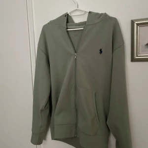 Polo Ralph Laruren mörk grön - Snygg grön huvtröja från Polo med dragkedja och broderad logga på bröstet. Tröjan har långa ärmar och en bekväm passform. Perfekt för en avslappnad stil.