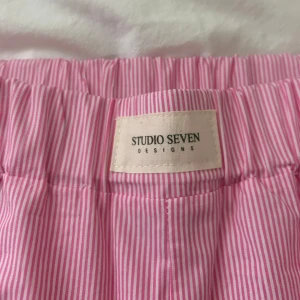 Rosa randiga byxor från Studio Seven Designs - Snygga rosa byxor med vita ränder från Studio Seven Designs. helt oanvända! raka i benen och bra passform förutom att de var lite tajta för mig runt lår/rumpa