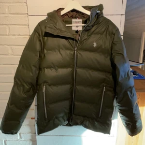 Olivgrön dunjacka från U.S. Polo Assn. - Säljer min olivgröna dunjacka från U.S. Polo Assn! med dragkedja och huva. Använd kanske 3-4 gånger, använder min andra jacka mera. Den är väldigt varm och skön, och skyddar bra från vind/kyla. Kostar 1600 ny. Skriv för fler frågor ⭐️
