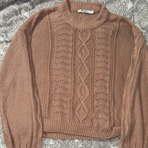 Rosa stickad tröja från NA-KD - Säljer en snygg Rosa stickad tröja från NA-KD med ett detaljerat mönster framtill. Tröjan har långa ärmar och ribbade kanter vid hals, ärmslut och nederkant. Perfekt för kyligare dagar!