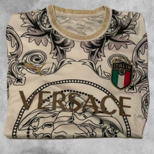 Beige fotbollströja från puma - Snygg beige fotbollströja från puma med ett iögonfallande mönster i svart och guld. Tröjan har korta ärmar och ett elegant märke med Italiens flagga på bröstet. Perfekt för den stilmedvetna fotbollsfantasten.