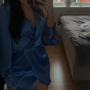 Blå i satin - Snygg blå omlottklänning i satin med långa ärmar och v-ringad design. Perfekt för en elegant look. 💙