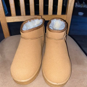 Bruna boots med foder - Säljer ett par bruna vinterskor med mjukt vitt foder. De har en enkel design med en liten flik baktill för lättare påtagning. Perfekta för kyliga dagar.