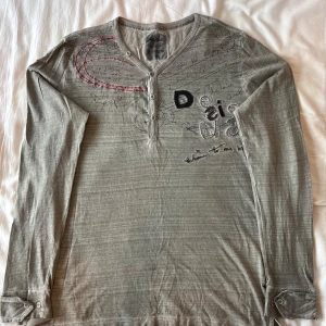 Unik Desigual långärmad T-Shirt - Gråaktig långärmad tröja från Desigual med unikt tryck och knappar vid halsen. Jättesnygg och unik i nyskick!