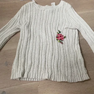 Vit ribbad tröja från H&M med broderad ros - Säljer en vit ribbad tröja från H&M med en vacker broderad rosdetalj på framsidan. Tröjan har långa ärmar och är perfekt för en stilren look. Passar bra till både jeans och kjol. 🌸