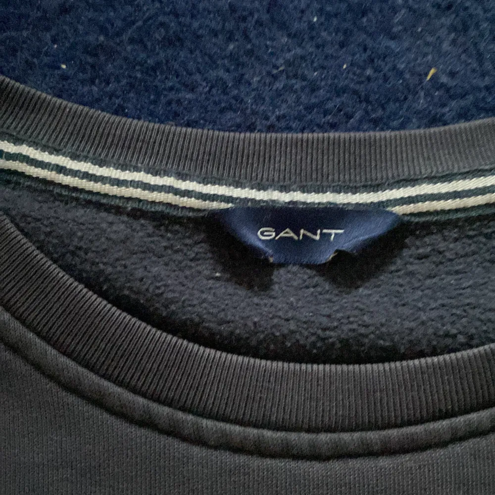 Säljer en stilren mörkblå sweatshirt från GANT med vit logotyp på framsidan. Tröjan har långa ärmar och en rund halsringning. Perfekt för en avslappnad stil.. Neuletakit & Villapaidat.