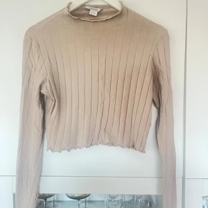 Beige ribbad tröja från Monki - Säljer en snygg beige ribbad tröja från Monki. Den är croppad och har långa ärmar, perfekt för en stilren look. Tröjan är i bra skick och passar både till vardags och fest. Superbekväm och lätt att matcha med andra plagg!