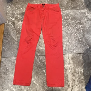 Röda byxor från H&M - Säljer ett par snygga röda chinos byxor från H&M i storlek 32/32. De har en klassisk design med knappar och dragkedja framtill. Perfekta för att liva upp garderoben med lite färg!