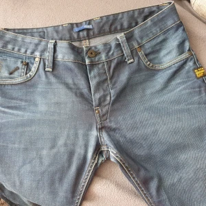 Blå jeans från G-Star - Säljer ett par snygga blå jeans från G-Star i storlek 36/32. De har en klassisk femficksdesign med coola detaljer på bakfickorna. Jeansen har en knappgylf och är i ett slitstarkt denimtyg. Perfekta för en casual look! Nypris runt 1600:-