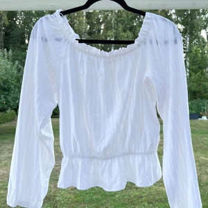 Långärmad vit topp - En vit långärmad topp från H&M. Använd max 5 gånger. Volang i nederkant och resår vid ärmsluten 🥰 Fint mönster i materialet och kan bäras både on/off shoulder 💞 Super-stretchig!!!  Längd: 43 cm Axel: 39 cm Byst: 85 cm