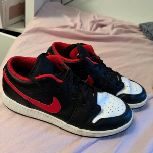 Nike Air Jordans i svart, röd och vit - Säljer ett par snygga Nike Air Jordans i svart, röd och vit. Skorna har en klassisk design med svart läder och röda detaljer, inklusive den ikoniska swoosh-loggan. De har en vit tåbox med perforeringar för extra ventilation. Perfekta för både vardag och fest!