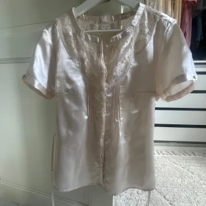 Blus i siden - Söt blus i siden, med spetsdetaljer och band som går att knyta både fram och baktill. Säljer då den inte kommer till användning. Obs Den översta knappen sakna!