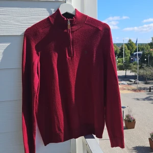 Röd merinoulltröja från Morris - Säljer en snygg och stilren röd tröja från Morris i 100% merinoull. Perfekt för höst och vinter med en dragkedja vid halsen för extra stil och komfort. Tröjan har långa ärmar och en liten broderad logga på bröstet. Passar både till vardags och festliga tillfällen!