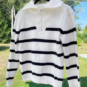 Vit/svart stickad tröja - En vit/svart randig stickad tröja med hög krage. Ribba krage med dragkedjestängning. Storlek L och passar lite fint oversized till mig som normalt har S 🩷 Använd max 3 gånger!  Längd: 62 cm Axel: 46 cm Byst: 104 cm Midja: 98 cm Kragens längd: 12 cm