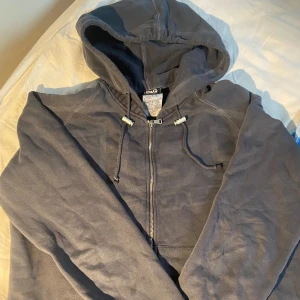 Blå hoodie från D&G - Säljer en snygg och bekväm blåhoodie från D&G. Den har en dragkedja framtill och en justerbar huva med snören. Perfekt till en ”laidback stil” eller för att hålla sig varm under kyliga dagar. Storlek M