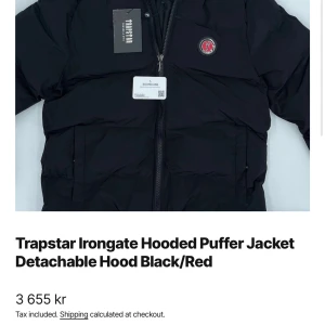 Trapstar Irongate Hooded Puffer Jacket - Säljer en snygg och varm pufferjacka från Trapstar med avtagbar huva. Jackan är svart med röda detaljer och har en cool Trapstar-logga på ryggen. Den är tillverkad i 100% polyester vilket gör den både lätt och bekväm. Perfekt för kalla dagar!