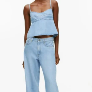 Ljusblå jeanslinnetopp med rosett - Superfin  ljusblå arket jeanslinnetopp  med smala axelband och en stor rosett i ryggen. Toppen är croppad och har en luftig passform,.  Öppen  ryggen med en söt rosett som detalj. Endast testad säljer för 700 + frakt 
