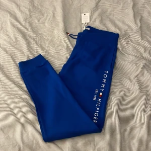 Blå mjukisbyxor från Tommy Hilfiger - Säljer ett par snygga blå mjukisbyxor från Tommy Hilfiger. De har en bekväm passform med resår i midjan och muddar vid bensluten. Byxorna har en stilren design med Tommy Hilfiger-loggan tryckt längs benet. Perfekta för en avslappnad dag hemma eller en snabb tur till affären.