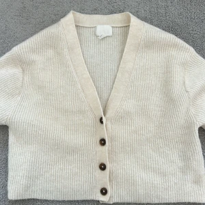 Lång armad stickad kofta  - Den här tröjan är ifrån H&M kids. Den är utslängd vid armarna där framme och är i storleken 146 till 152 . Den är ljus beige och är mysigt till både hösten och sommaren . Kan vara lite croppad så är inte så lång . 