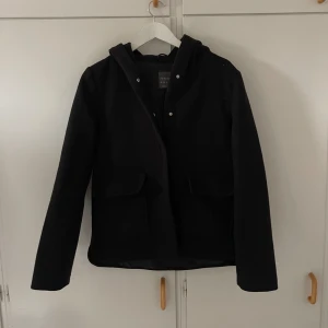 Svart jacka med huva - Säljer en stilren svart jacka med huva. Den har långa ärmar och praktiska fickor framtill. Perfekt för höst och vår när det är lite kyligt ute. Jackan är i bra skick och passar till de flesta outfits.