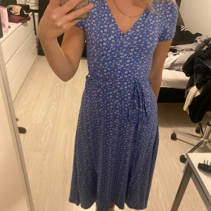 Blommig klänning - Blå vit blommig sommar klänning, som är asymmetrisk  Välanvänd  95% polyester  5% spandex Köpt på gekås, Ullared 