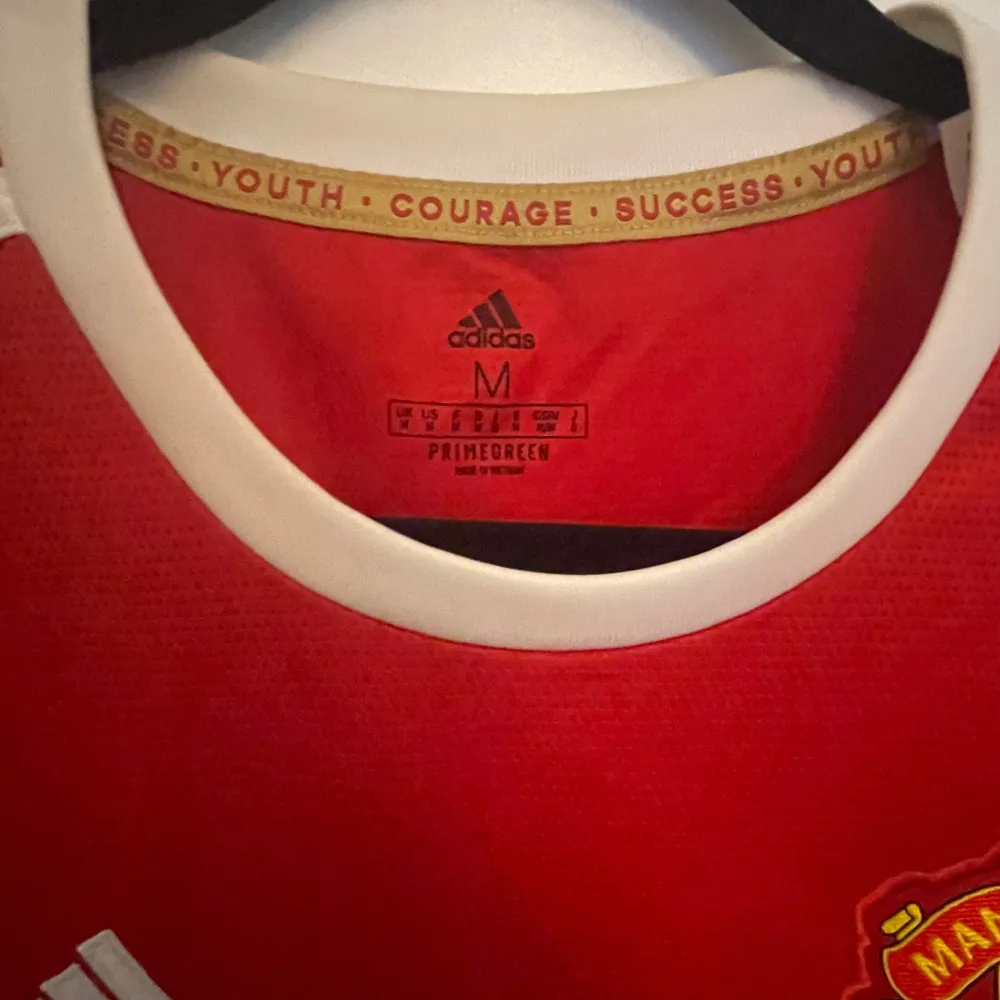 Säljer en snygg röd Manchester United fotbollströja från Adidas. Tröjan har korta ärmar och är i nyskick. Den har vita detaljer och klubbens emblem på bröstet. Autentisk . T-shirts.