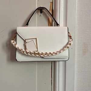 Vit fräsch handVäska med guld detaljer  - En vit fin handväska 20cm bred 14 cm höjd.