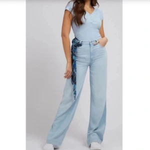 Ljusblå jeans från Guess - Säljer ett par snygga ljusblå jeans från Guess. De är högmidjade och har en loose passform med en cool scarf-detalj i midjan. Perfekta för en avslappnad men stilren look. Passar bra till både sneakers och klackar!