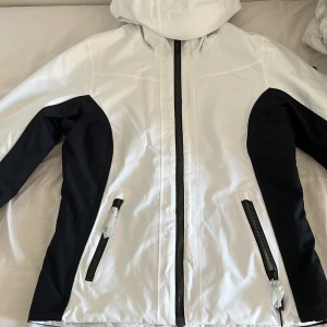 Skidjacka - En svartvit skön, varm skidjacka från märket Everest med luva och flera fickor. Jackan är oanvänd och har fortfarande sitt prislapp kvar.