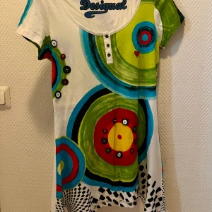 Färgglad klänning från Desigual - Säljer en superhärlig och färgglad klänning från Desigual! Den har ett unikt mönster med stora cirklar i grönt, blått, rött och gult. Klänningen är kortärmad och har en rund halsringning med knappar. Perfekt för en somrig dag eller en fest där du vill sticka ut!