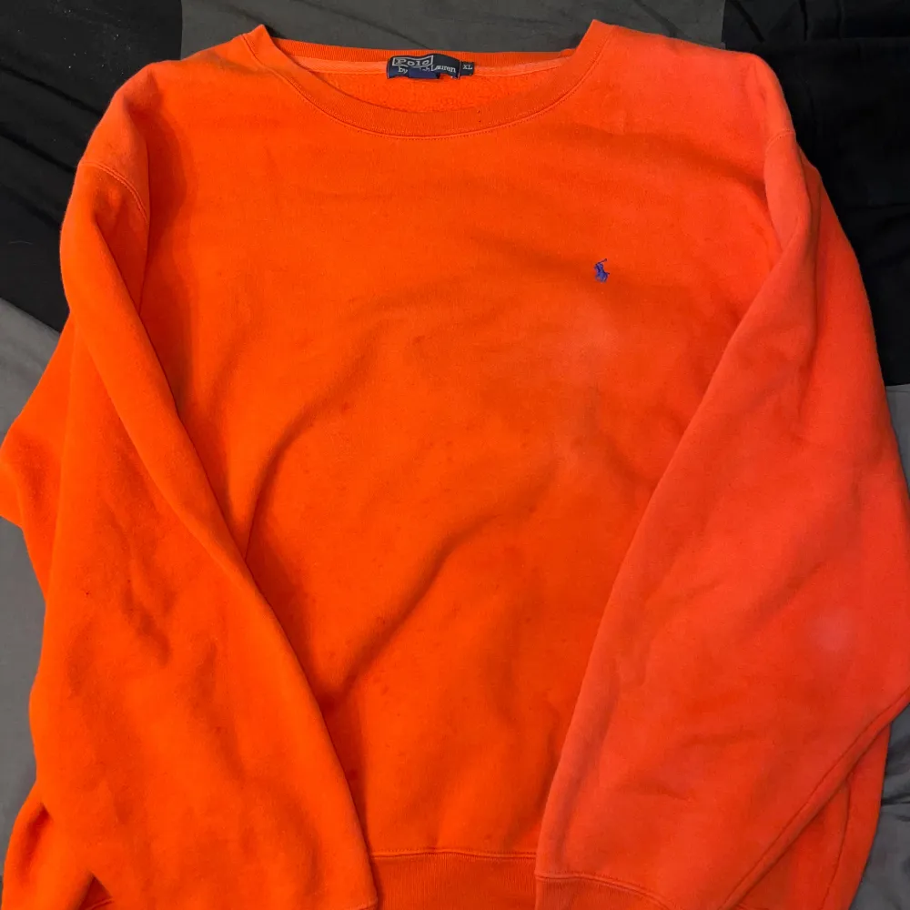 Säljer en snygg och färgglad orange tröja från Polo Ralph Lauren. Den har en klassisk design med rund hals och långa ärmar. Tröjan är i bomull och har den ikoniska lilla loggan broderad i blått på bröstet. Perfekt för en casual look!. Tröjor & Koftor.