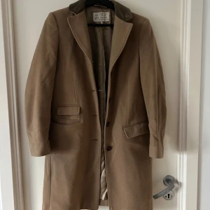 Beige kappa från Newhouse - Säljer en elegant beige kappa från Newhouse. Den har en klassisk design med knappar framtill och två fickor. Perfekt för höst och vår, och ger en stilren look. Storlek 34, vilket motsvarar dam XS. Kappan är i bra skick och redo för nya äventyr!