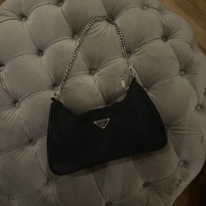 Svart axelväska med kedja - Snygg svart axelväska med en stilren kedja som axelrem. Väskan har en dragkedja upptill och är perfekt för både vardag och fest. Den är kompakt men rymmer det viktigaste. Perfekt för att ge din outfit en elegant touch!