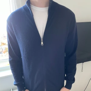 Mörkblå tröja med dragkedja från S&T Clothing - Säljer en stilren mörkblå tröja från S&T Clothing i storlek M. Den är gjord av en blandning av merinoull och kashmir, vilket gör den supermjuk och bekväm. Nypris runt 1200.