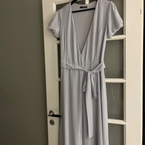 Ljusblå långklänning med knytband - Säljer en elegant ljusblå långklänning med v-ringning och korta ärmar. Klänningen har ett fint knytband i midjan som ger en smickrande passform. Perfekt för sommarens fester eller en stilren vardagslook.