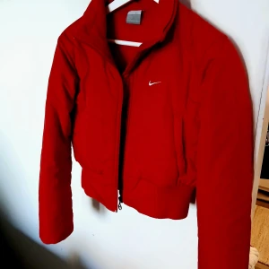 Röd dunjacka från Nike - Säljer en snygg röd dunjacka från Nike i storlek S. Jackan har en dragkedja framtill och en liten Nike-logga på bröstet. Perfekt för kyliga höst- och vinterdagar. Den är i mycket bra skick och redo för nya äventyr!
