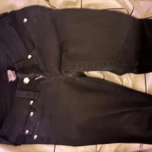 Svarta lågmidjade bootcut true religion jeans - Säljer ett par svarta jeans från Brand Jeans i storlek 26. De har en klassisk femficksdesign med diamant liknande knappar knappar och en snygg bakficka med dekorativ söm. Perfekta för både vardag och fest!